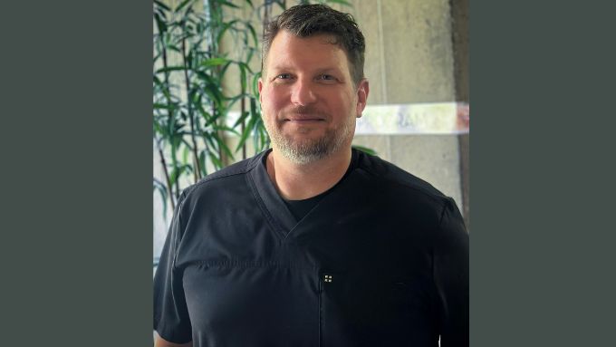 Middle aged white man wearing black scrubs with a tree in the background