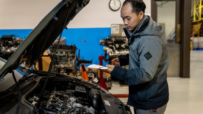 Asian man in dark gray hooded jacket works on a car in a shop