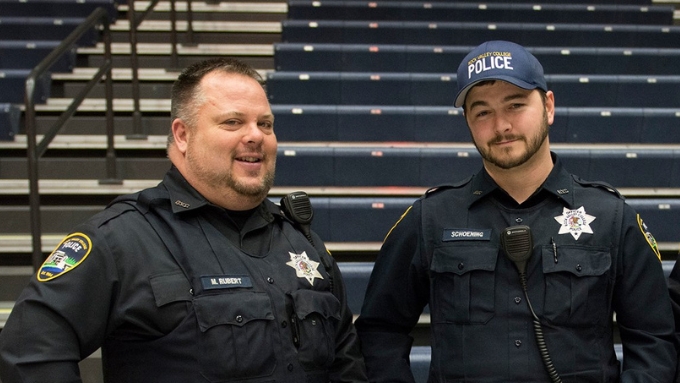 two white male uniformed police officers stand in front of the bleachers 
