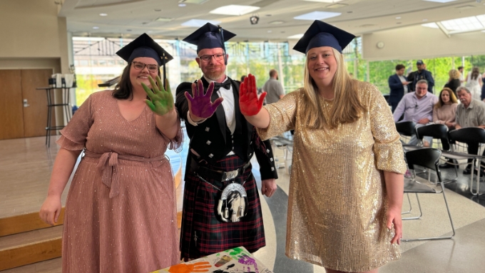 three massage therapy grads stand with their panted palms ofacing the camera