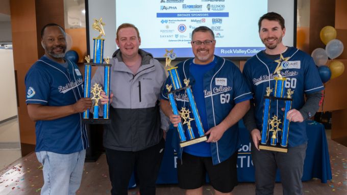 Four men (one African American man on left, three Caucasian on right) holding trophies wearing blue RVC jerseys and warm gear.