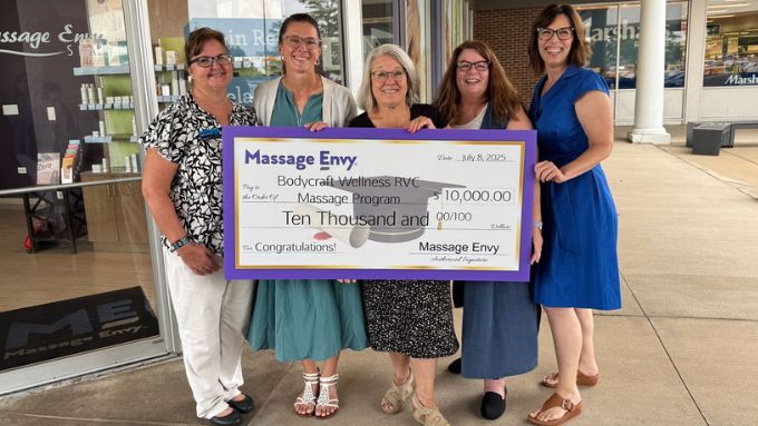Five women holding up a large donation check in front of Massage Envy storefront
