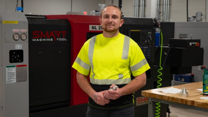 Young white man wearing a yellow safety shirt standing in from of CNC machines