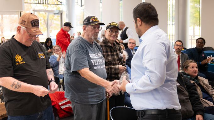 three older male veterans stand to accept medallions for their service while people around them are seated and applaud