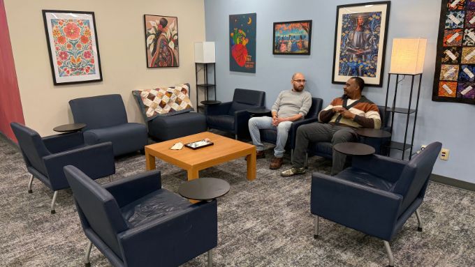 A white male and African American make seated in a room surrounded by art