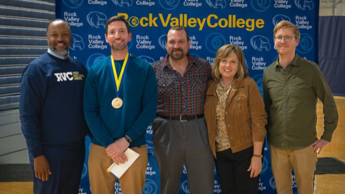 five adults (one older black man, three white men, and one white woman) stand in front of a Rock Valley College backdrop