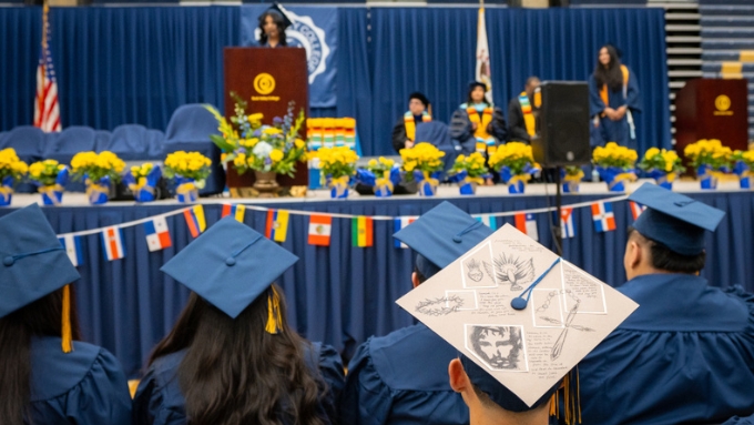 a diverse group of graduates face the stage and watch someone at a podium speak