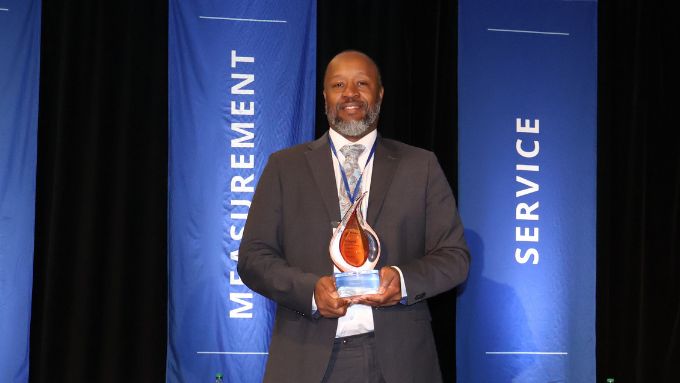 African-American man in a dark gray suit holds a glass award statuette
