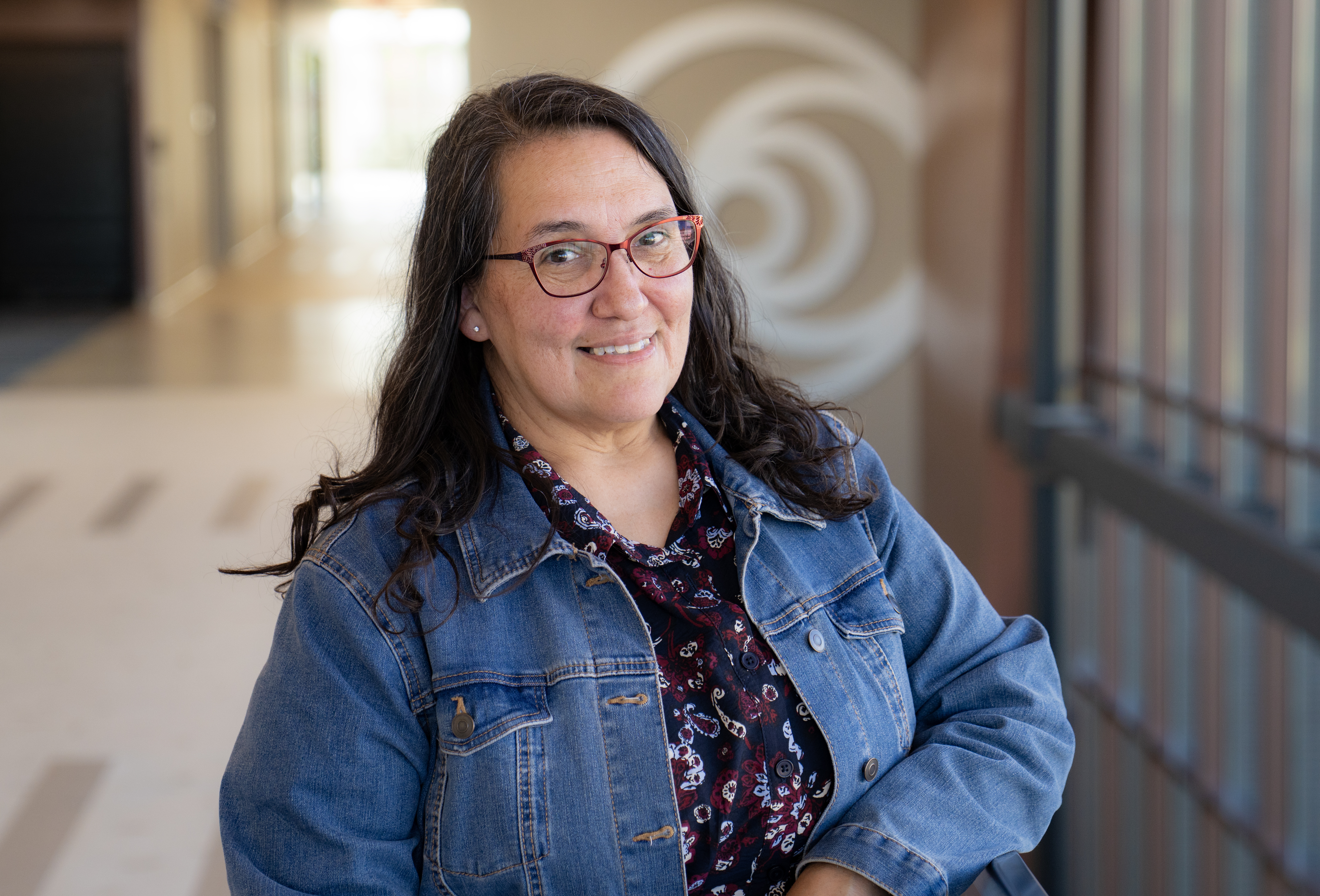 Woman with long dark hair wearing glasses and jean jacket with blue floral top at DTW