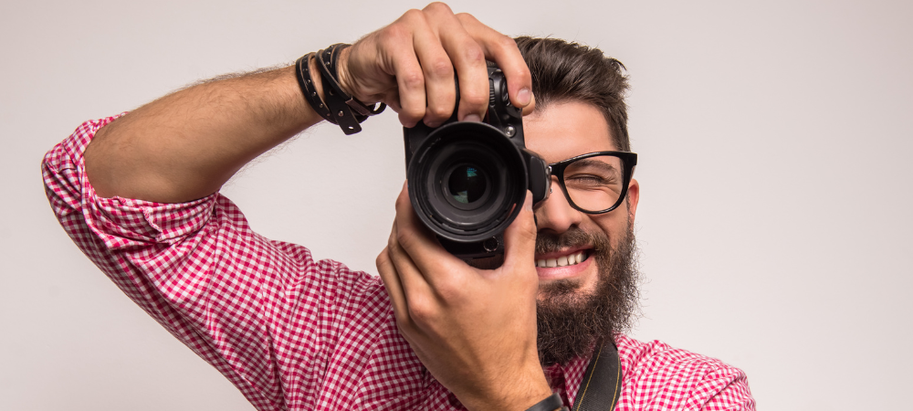 man wearing red plaid top holding camera in front of face