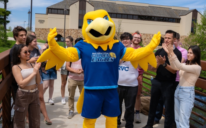 college mascot Arvee posing with students on campus bridge
